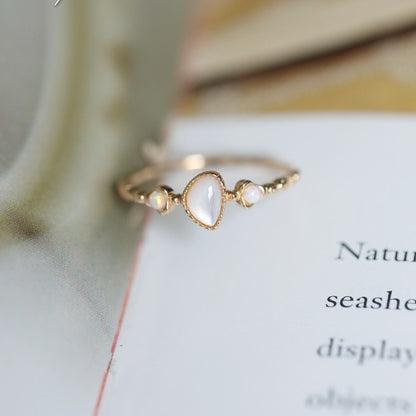 Dainty gold-tone ring with teardrop white cabochon and two opal accents on an open book
