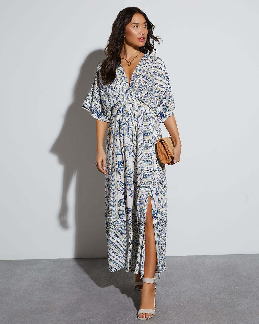 Full length ivory and cobalt paisley maxi dress, front view with a straw clutch, White blue variant