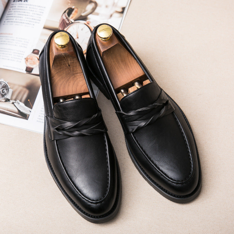 Black loafers in pebble grain finish laid on beige fabric, braided cords knotted at the strap sides