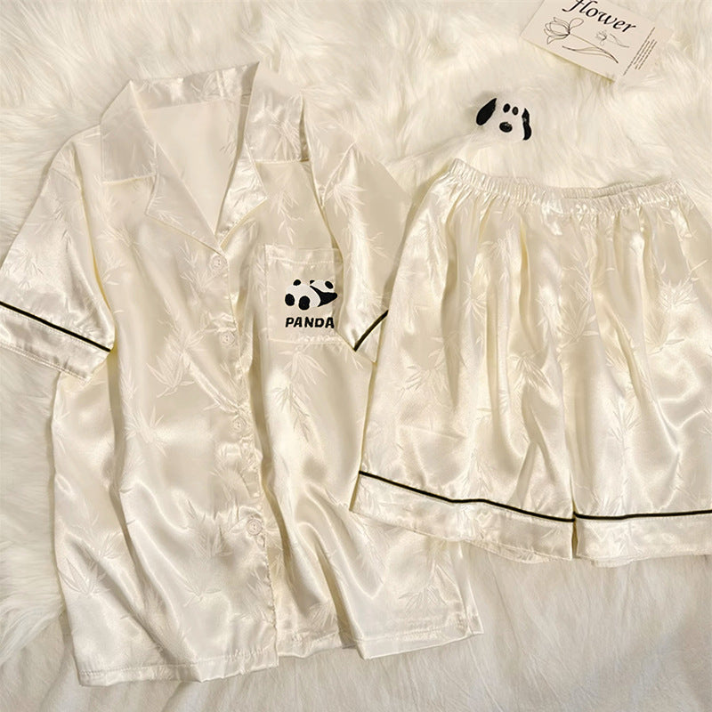 Cream ice silk pajama set with black piping and a panda chest pocket on a white fluffy rug, size XL