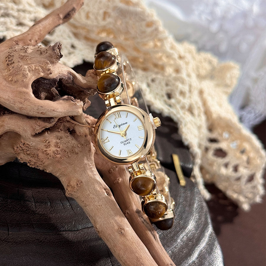 Gold tone quartz watch on a tiger eye stone beaded bracelet resting on driftwood