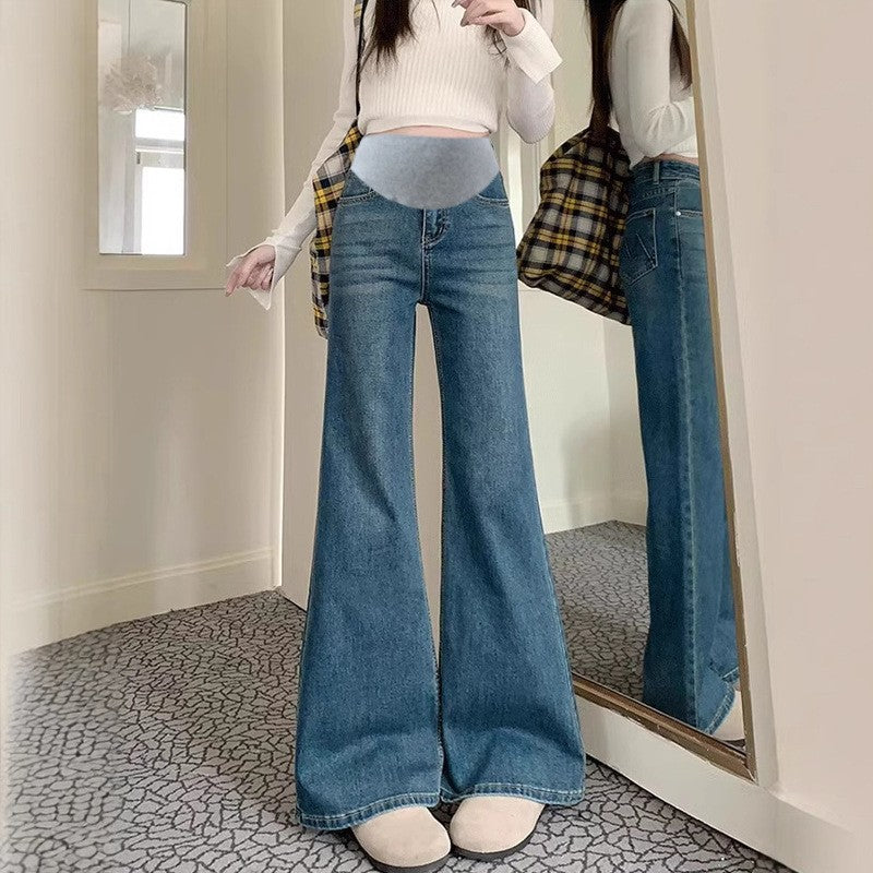 Medium blue flared maternity jeans with a gray stretch belly panel, worn with a white crop top next to a mirror