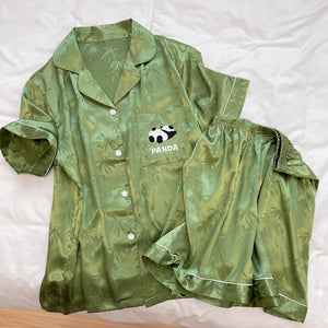 Green short sleeve pajama shirt with white piping and matching shorts laid flat on a bed