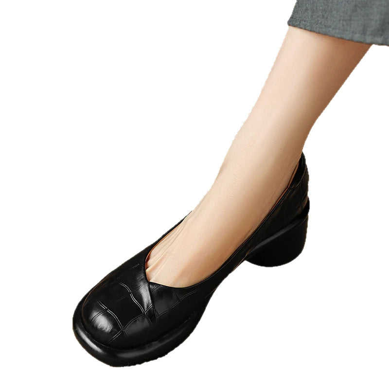 Black embossed leather slip-on shoe with a round block heel worn on a foot, on a white background