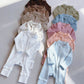 Baby rompers laid in two columns on a gray floor, from chocolate brown to white, olive, blue, pink and sky blue