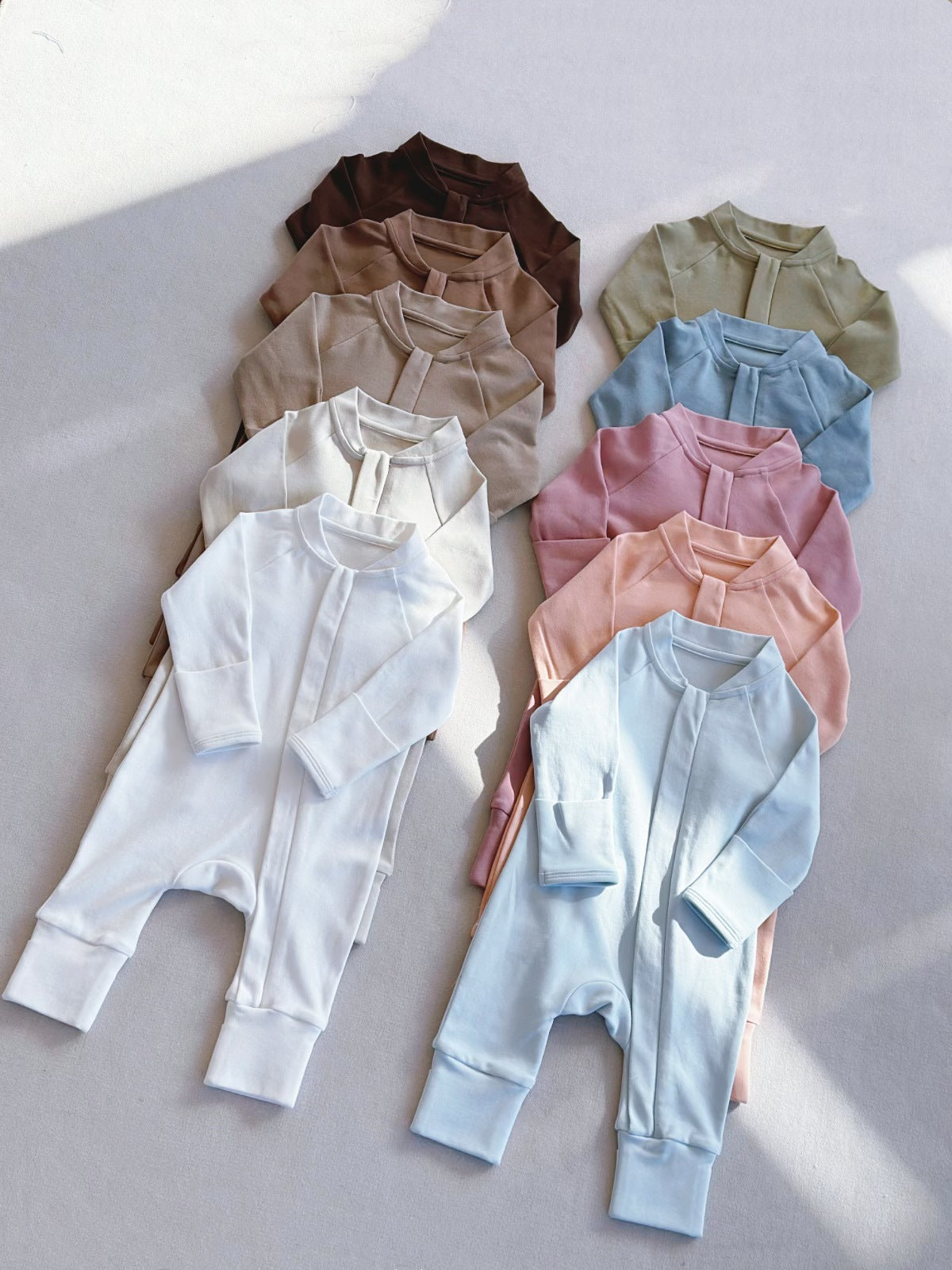 Baby rompers laid in two columns on a gray floor, from chocolate brown to white, olive, blue, pink and sky blue