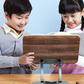 Two children reading an open book resting on the wood-grain board of the adjustable reading stand