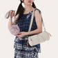 Woman in a plaid dress wearing a cream cylindrical nylon shoulder bag and holding a small lilac drawstring pouch