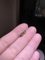 Pair of small round green cabochon stud earrings in silver tone four prong settings held on fingertips