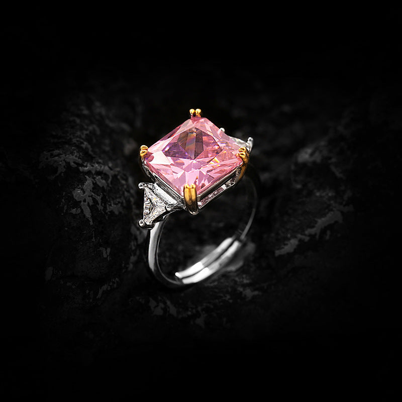 Large pink radiant stone in gold toned prongs with clear trillion accents, dark rock background