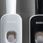 Grey and black toothpaste dispensers on a wall with a brush loaded under the grey unit window