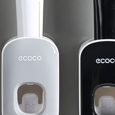 Grey and black toothpaste dispensers on a wall with a brush loaded under the grey unit window