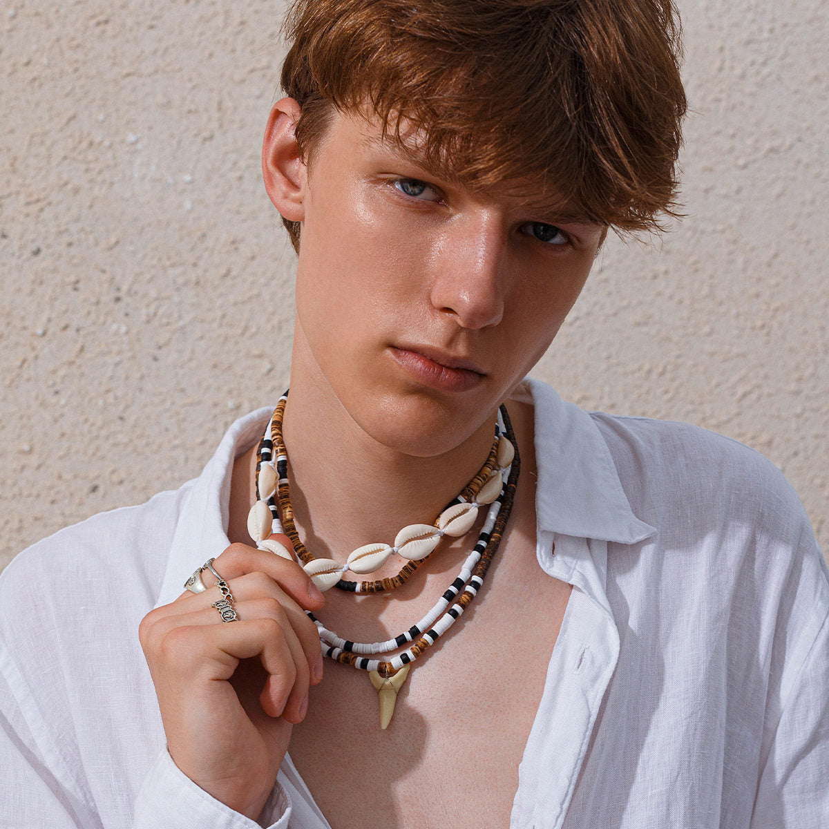 Man in an open white shirt wearing the four strand cowrie shell necklace set with the tooth pendant