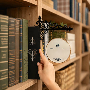 Hand sliding the black iron plate between books with a round hanging sign plaque