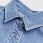 Close view of a pointed denim collar with contrast topstitching and two metal buttons on a washed blue jacket