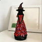 Red variant with purple leaf tips: witch statue in a red gown on a white shelf with a picture frame