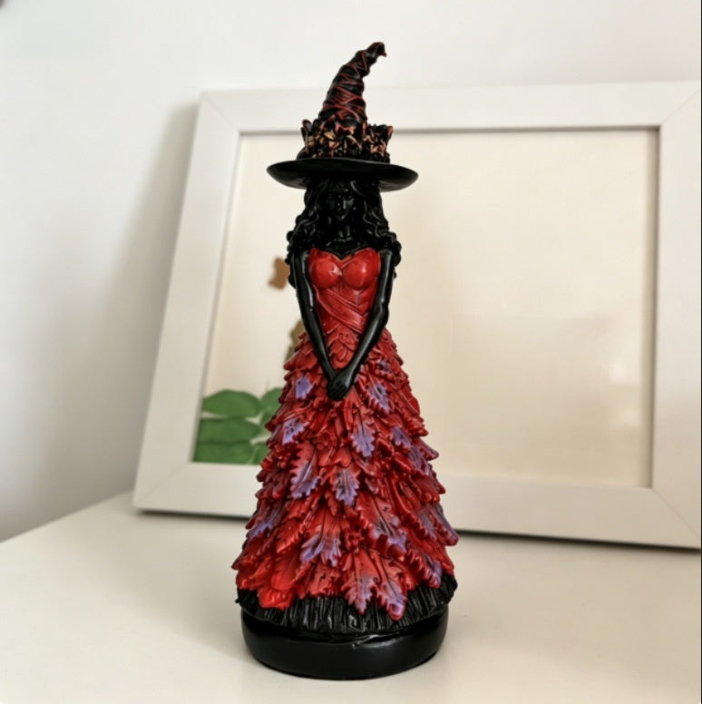 Red variant with purple leaf tips: witch statue in a red gown on a white shelf with a picture frame