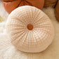 Beige round pleated plush throw pillow with an orange centre button on a fluffy white throw, beige textured zafu variant