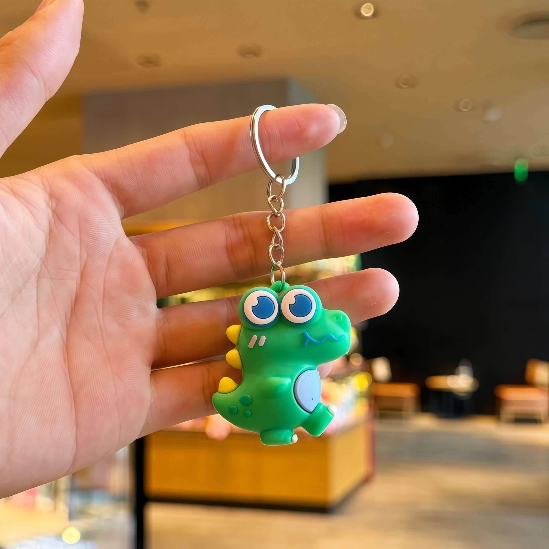 Cartoon dinosaur keychain charm hanging from a bag zipper pull