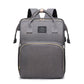 Gray diaper backpack front view with two top handles, a woven label, a front zip pocket and padded back straps