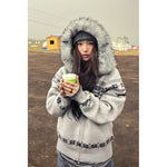 Grey Fair Isle knit cardigan with faux fur hood zipped on a woman holding a paper cup, front view