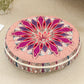 Round cushion with a magenta pink mandala print top and a pink striped side, on a beige rug