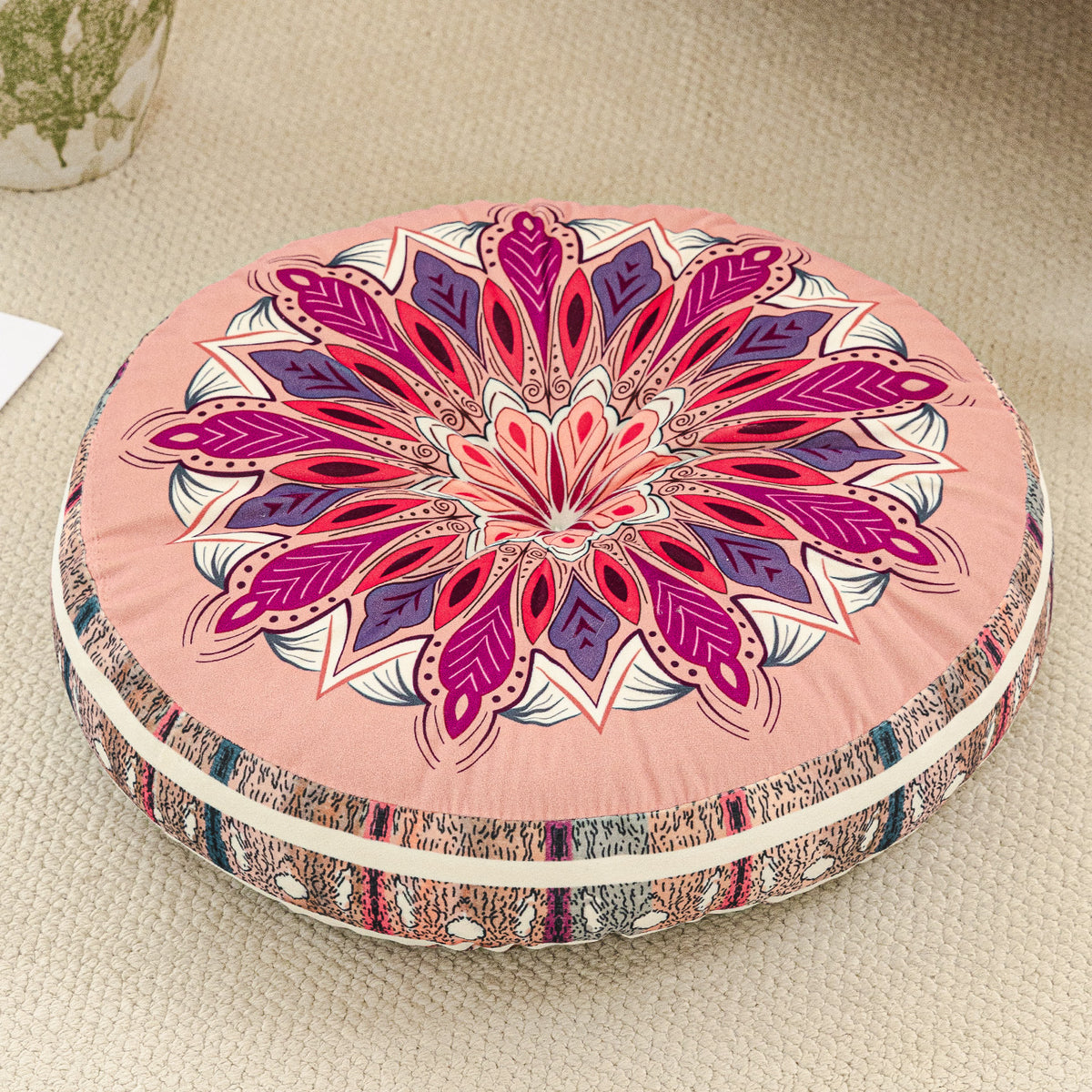 Round cushion with a magenta pink mandala print top and a pink striped side, on a beige rug