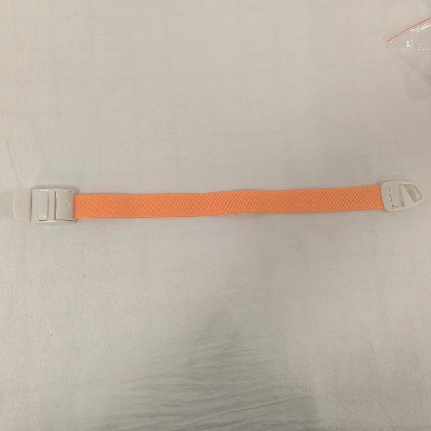 Single orange elastic quick release tourniquet band with a white snap buckle laid flat