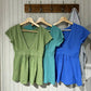 Three short-sleeve V-neck tops in green, teal and royal blue hanging on wall hooks