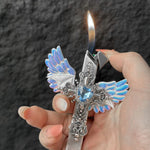 Hand lighting the angel wings cross lighter with a flame rising from the top, on a dark stone background