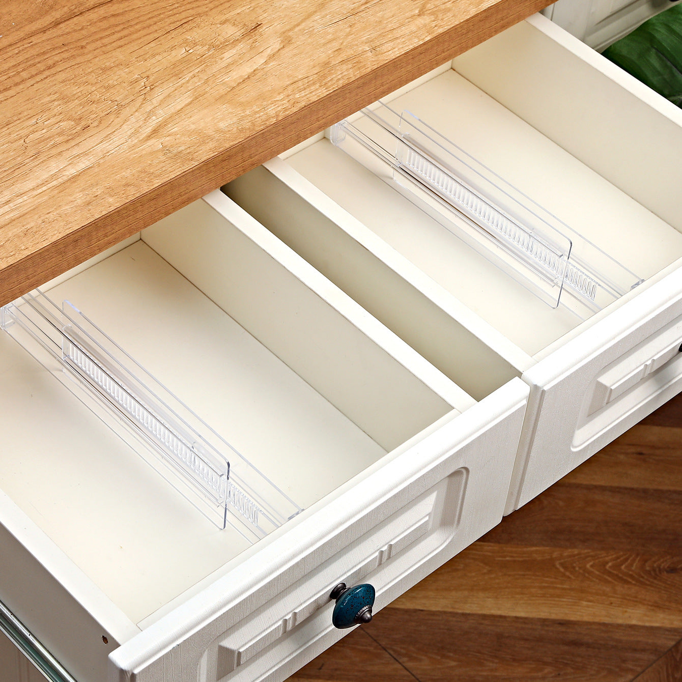 Clear drawer dividers separating folded shirts and rolled socks inside a wooden drawer