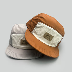 Grey and camel flat brim camp caps stacked, cream contrast panels and Adventure leather patch in view