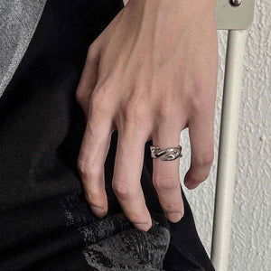 Sculpted flame stainless steel band worn on the ring finger of a hand against a black sleeve and a white wall
