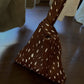Brown triangle knot handle pouch bag with cream spots and a looped handle standing on a wooden table