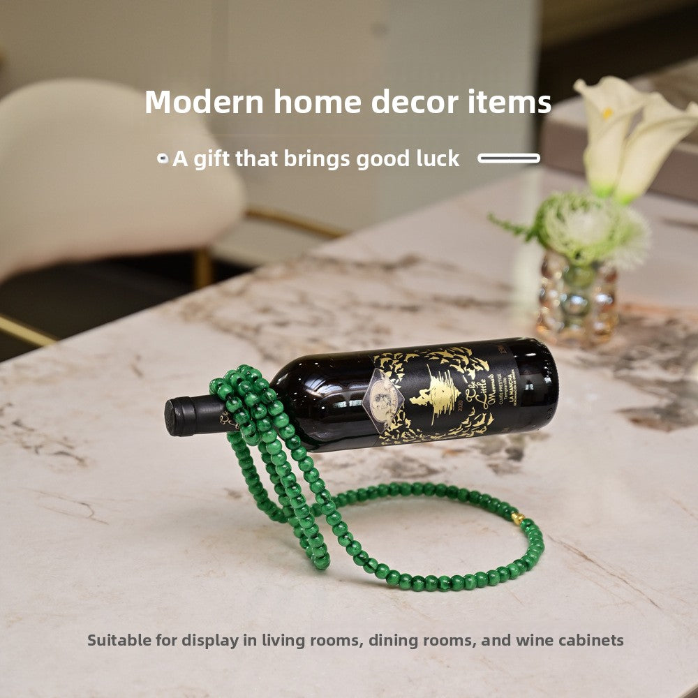 Green beaded wine bottle holder balancing a wine bottle on a marble table beside a white calla lily