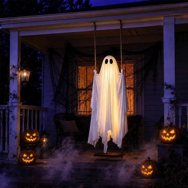 Glowing white ghost on a rope swing hung on a porch at night beside carved pumpkins and fog