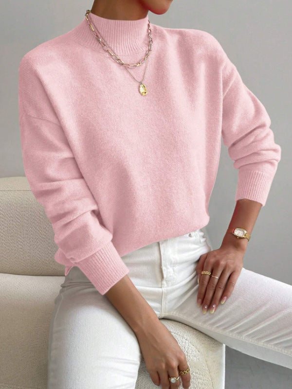 Woman wearing a pink half-high neck pullover sweater with long sleeves and ribbed cuffs seated on a sofa