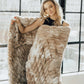 Woman by a large window holding up a ruched tie-dye brown plush blanket draped over her shoulder