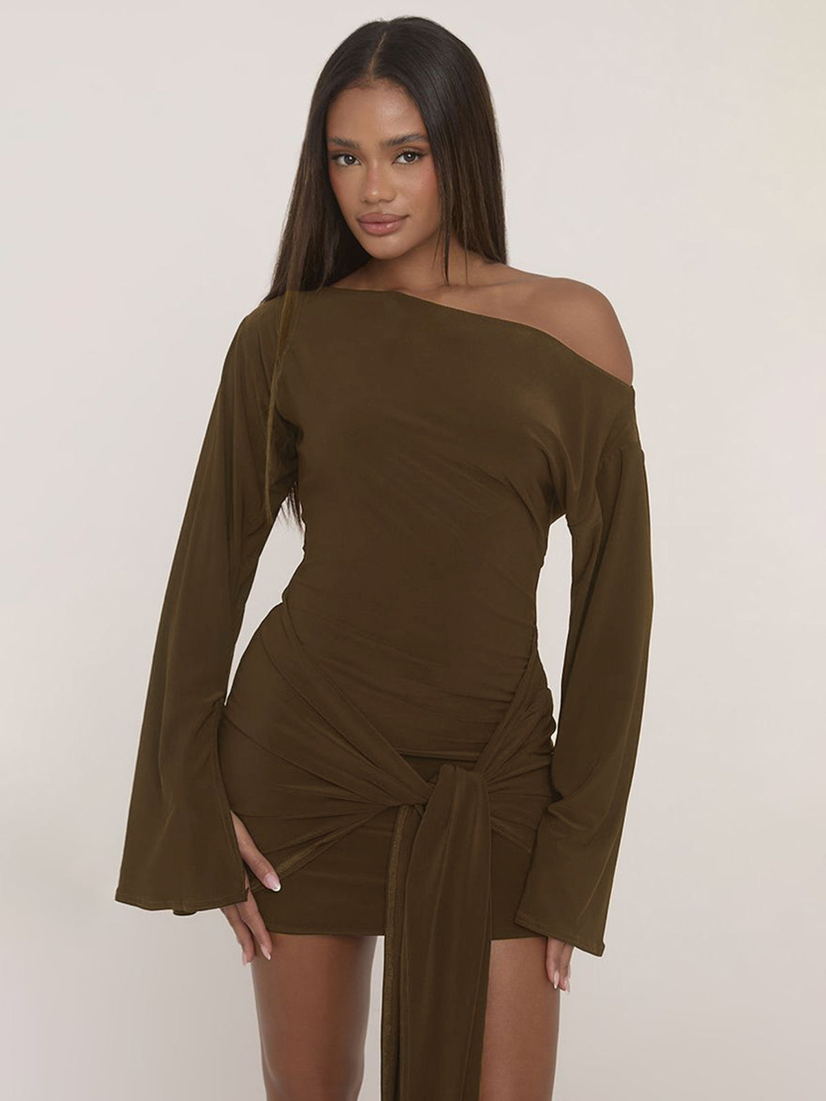 Woman in an olive brown long bell sleeve mini dress with a slanted shoulder neckline and a knot at the hip