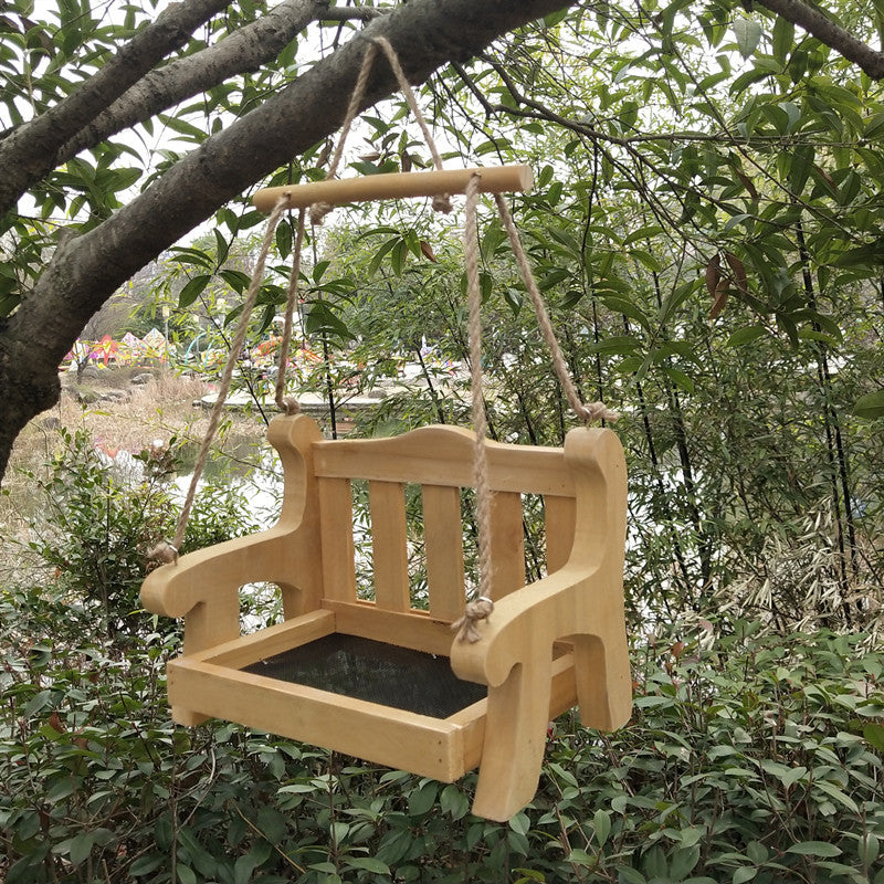 Natural wood bench bird feeder with a mesh floor and a wooden crossbar hanging in a green garden