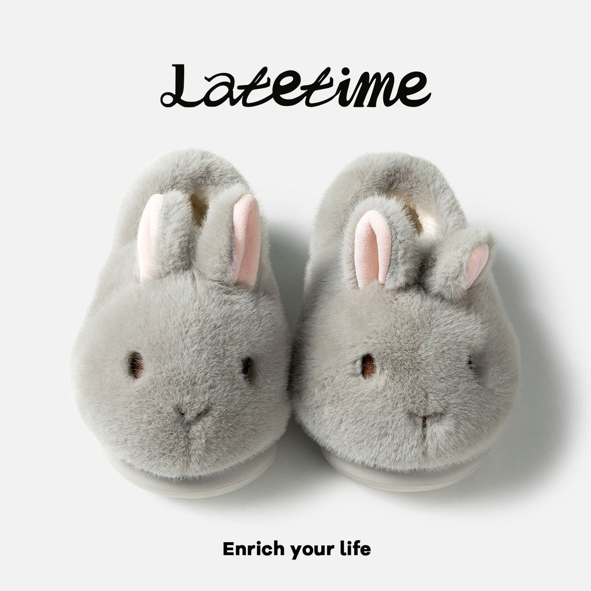 Pair of gray bunny plush slippers with pink inner ears seen from above on a light panel with script lettering, view 1 of 3