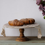 Wooden pedestal cake stand holding croissants beside dried roses on a rustic table