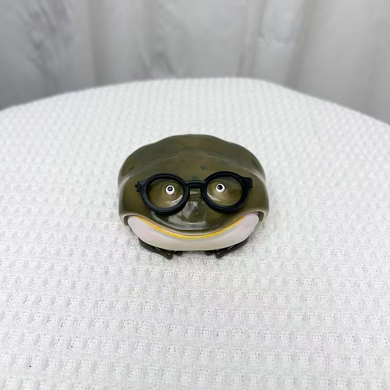 Olive resin frog earbud case wearing round black spectacles, closed, on a white cloth