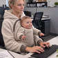 Cream teddy fleece hoodie with a baby at the chest while the mother types at an office desk
