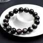 Round gold sheen obsidian beads strung on an elastic bracelet on dark surface