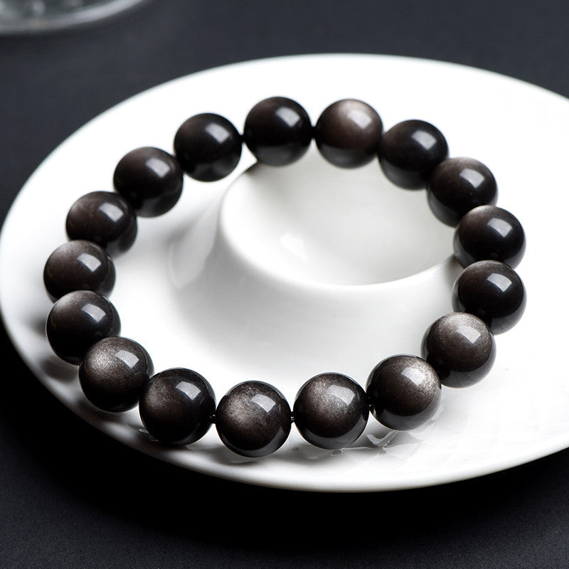 Round gold sheen obsidian beads strung on an elastic bracelet on dark surface
