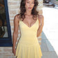 Yellow strappy jersey mini dress front view against a stone wall in daylight