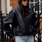 Woman in a red cap and sunglasses wearing a short black PU leather moto jacket over jeans