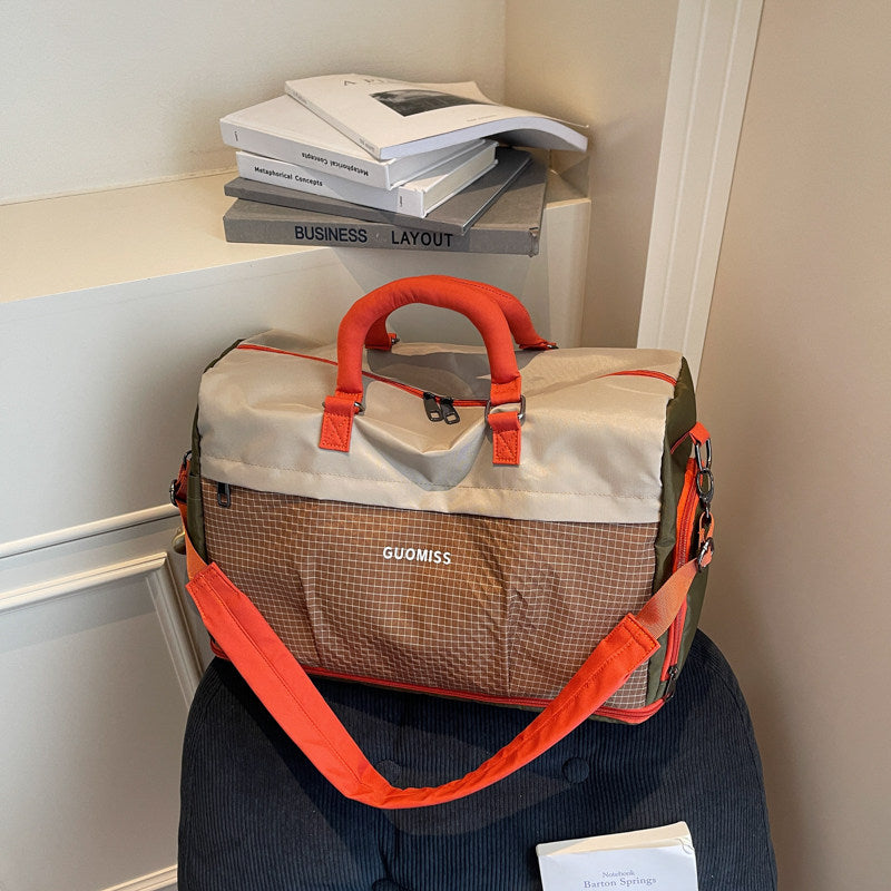 Beige brown and orange travel duffel with a grid front pocket resting on a dark stool