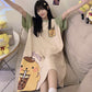 Woman raising both arms on a sofa in a cream short sleeve nightgown with green sleeves and a yellow dog print on the hem